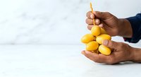 Close-up of hands holding fresh yellow lemons against white marble background. Suitable for food, health, cooking, and wellness marketing materials.