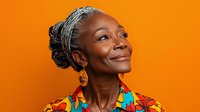 Mature African American woman with gray hair in colorful floral top smiling confidently against vibrant orange background, radiating joy and wisdom in studio portrait.