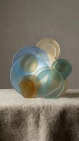 Abstract glass circles in blue, green and amber tones arranged as modern art sculpture on textured surface with soft lighting for contemporary design.