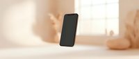 Smartphone with blank black screen floating in air against blurred beige interior background with natural window light, suitable for app mockups and digital marketing.
