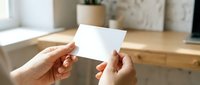 Hands holding blank white business card mockup template for branding design presentation in modern office workspace environment.