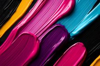 Vibrant cosmetic smears of lipstick or cream texture in pink, purple, yellow and blue colors on black background, macro photography showing glossy surface.
