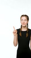Young woman with braided brown hair and fair complexion wearing black sleeveless dress, pointing upward with thoughtful expression against white background for advertising and promotional use.
