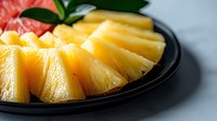 Fresh juicy pineapple slices arranged on black plate against light background, close up view of tropical fruit with vibrant yellow color and texture.