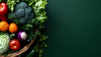 Fresh organic vegetables and fruits in woven basket on dark green background, including broccoli, lettuce, tomatoes, oranges and cabbage. Top view food composition.