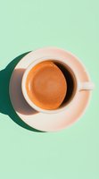 White coffee cup with fresh espresso on mint green background casting dramatic shadow, minimalist overhead composition for food and beverage marketing.