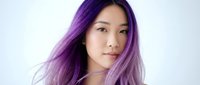 Young Asian woman with vibrant purple hair looking at camera with natural makeup and confident expression isolated on white background for beauty concepts.