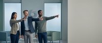 Business team of three professionals pointing forward in modern office meeting room with copy space for corporate planning and teamwork concepts.