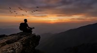 Young man hiker sitting on mountain cliff edge during golden sunset with birds flying overhead. Adventure travel and meditation concept for outdoor lifestyle.