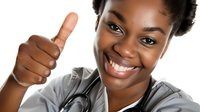 Young African American female healthcare worker in scrubs and stethoscope showing thumbs up with bright confident smile against white background.