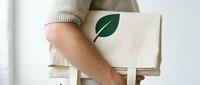 Person holding a natural canvas tote bag with a green leaf print, promoting eco-friendly lifestyle and sustainable shopping choices.