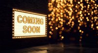 Illuminated coming soon marquee sign with golden bokeh lights creating anticipation atmosphere for business opening announcement and promotional campaigns.