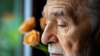 Elderly man with white hair and mustache in peaceful meditation pose with closed eyes, orange roses in soft focus background creating serene atmosphere.