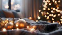 Cozy winter evening with silver ornaments and string lights on gray knitted blanket against blurred Christmas tree lights creating warm bokeh atmosphere.