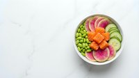 Fresh poke bowl with salmon, edamame, cucumber, and watermelon radish on white marble background, top view with copy space.