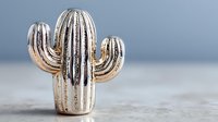 Golden metallic cactus decoration on wooden surface against blue background. Modern home decor accent piece for contemporary interior design styling.