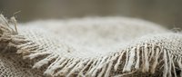 Natural burlap fabric with frayed edges and loose threads, rustic textile material for crafting, packaging, and eco-friendly design projects.