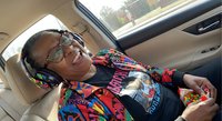 Elderly African American man wearing colorful patterned shirt relaxing in luxury car interior during road trip or travel journey.