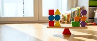 Colorful wooden geometric blocks and educational toys scattered on bright classroom floor with natural sunlight streaming through windows.