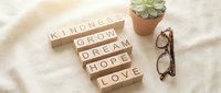 Wooden letter blocks spelling kindness, grow, dream, hope, love on soft white surface with succulent plant and glasses, motivational lifestyle concept.