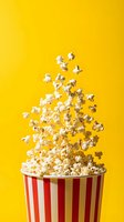 Fresh popped corn kernels flying from red striped container on bright yellow background for movie theater and entertainment concepts.