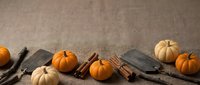Autumn harvest display with orange and white pumpkins, cinnamon sticks, and rustic wooden boards on burlap background for seasonal decorating.