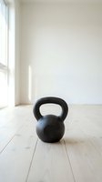 Black kettlebell on light wooden floor in bright, minimalist gym space with white walls and natural window light, suitable for fitness and wellness content.