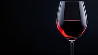 Red wine in elegant glass against dark background, dramatic lighting highlights liquid's rich color and crystal clarity. For restaurant menus and beverage marketing.