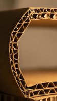 Corrugated cardboard edge showing honeycomb structure detail in warm lighting for packaging and shipping industry applications.