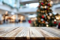 Empty wooden table with blurred Christmas shopping mall background, decorated tree with bokeh lights for product display during holiday season.