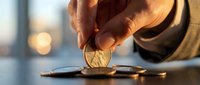 Hand placing golden coin into piggy bank slot for savings and financial planning goals with warm lighting background.