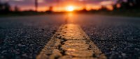 Close-up view of asphalt road with yellow center line at sunset, low angle perspective capturing warm golden light reflecting on pavement surface for travel and transportation concepts.