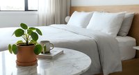Modern minimalist bedroom interior with white bedding, marble table, houseplant and natural light creating serene atmosphere for home decor inspiration.