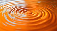 Concentric ripples forming spiral pattern on orange liquid surface with dynamic wave motion and light reflection creating mesmerizing abstract background.