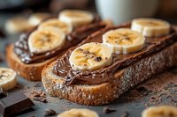 Chocolate spread on toasted bread topped with fresh banana slices and cocoa powder for breakfast or snack time.