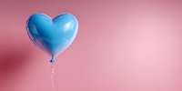 Blue heart-shaped balloon floating against soft pink background, creating romantic contrast for celebration or love concept.
