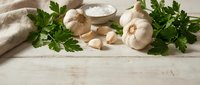 Fresh garlic bulbs and cloves with green parsley and sea salt on rustic white wooden table, copy space for food and cooking content.