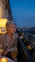 Mature Caucasian woman relaxing on luxury hotel balcony at twilight with city lights and wine glass creating elegant evening atmosphere for lifestyle content.