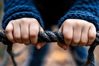 Child's hands gripping dark rope, wearing blue knitted sleeves. Outdoor play, strength training, or playground activity concept for youth development and physical fitness.