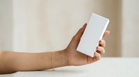 Man with dark skin tone holding blank white rectangular box or product packaging against neutral beige background for branding and marketing mockups.