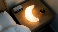 Glowing crescent moon night light on wooden bedside table creates cozy bedroom ambiance for relaxation and sleep.