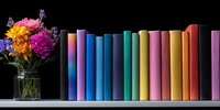 Colorful book spines arranged in rainbow order on white shelf with fresh flowers in glass vase, creating cozy reading atmosphere against dark background.