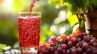Fresh red grape juice pouring into glass with ripe grapes and vineyard background in golden sunlight for healthy lifestyle and natural beverage concepts.