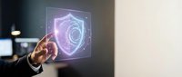 Businessman hand touching holographic cybersecurity shield icon in modern office environment for digital protection and data security solutions.