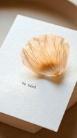 Dried flower petal resting on a white textured card with be kind typewriter text, warm neutral tones, minimal aesthetic for stationery and lifestyle design.