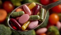 Colorful vitamins and dietary supplements in metal spoon with fresh fruits and vegetables background for healthy lifestyle and nutrition concept.