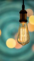 Vintage Edison bulb glowing with warm filament against blurred bokeh lights background for creative lighting design and retro interior decoration concepts.