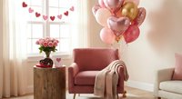 Cozy living room decorated for Valentine's Day with pink armchair, heart balloons, roses and romantic garland creating warm festive atmosphere.