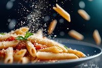 Penne pasta with tomato sauce and parmesan cheese sprinkled from above, creating dynamic food composition on dark background with flying ingredients.