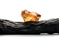 Raw amber crystal glowing with warm light on dark textured stone surface against white background, dramatic contrast highlighting natural mineral formation.